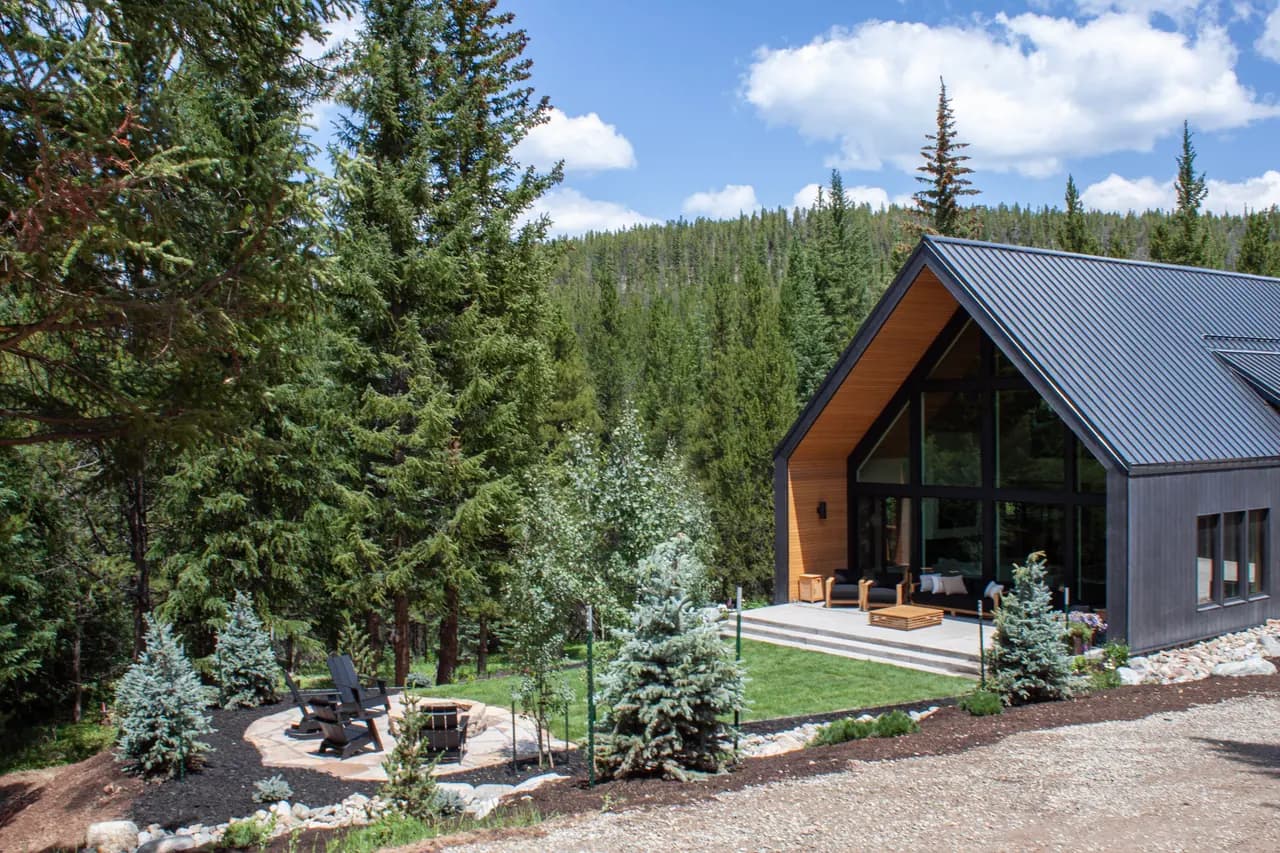 Modern black A-frame cabin with a lawn and fire pit patio among pine trees