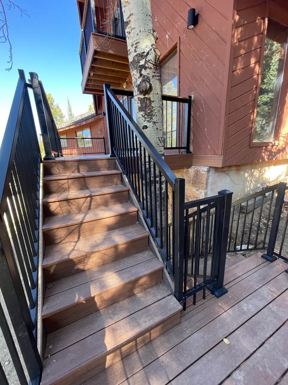 Composite deck stairs with black metal railings beside an aspen tree